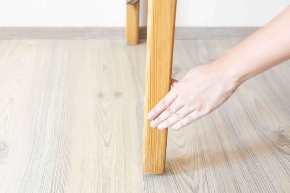 Hand checking an uneven wooden table leg on a light wood floor