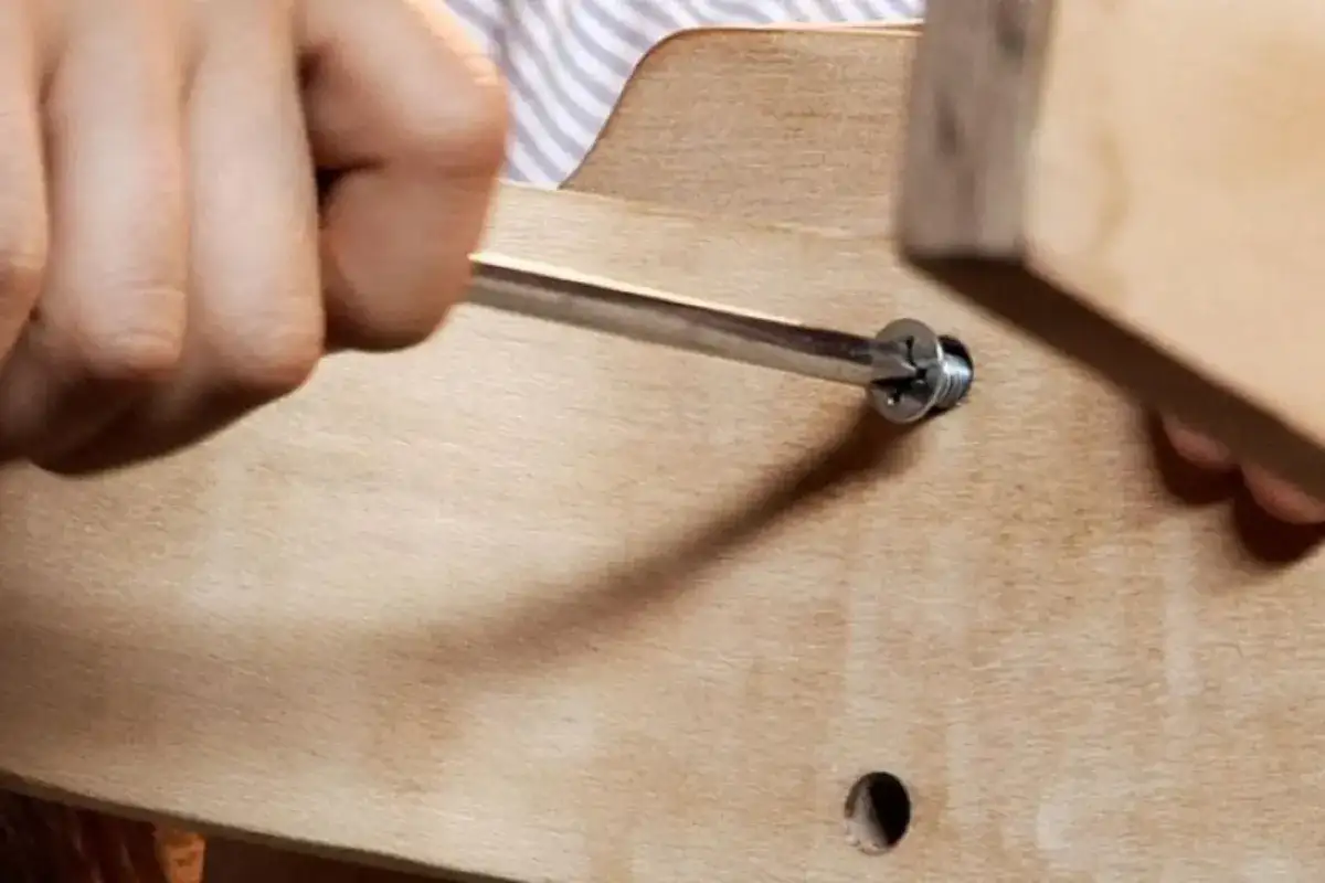 Hand using a screwdriver to tighten a screw under a wooden table frame