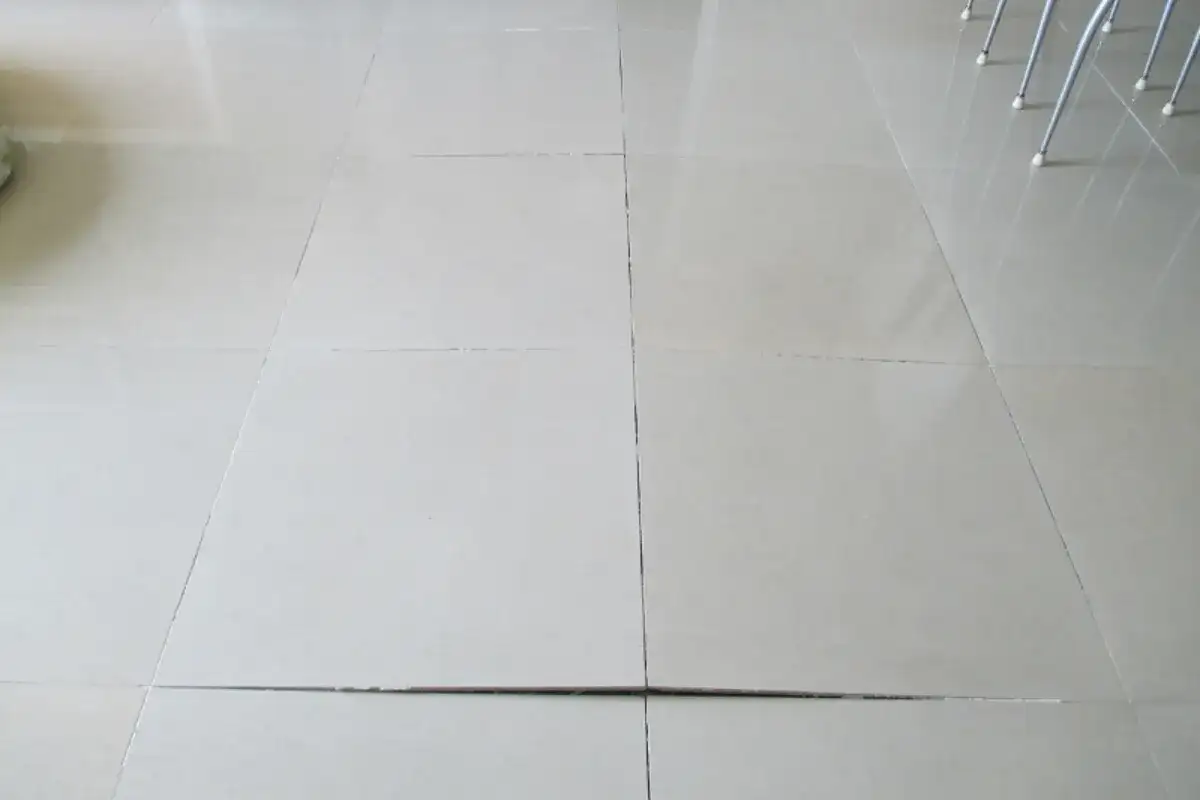 Uneven tiled floor with visible gaps and raised edges causing an unstable surface for furniture