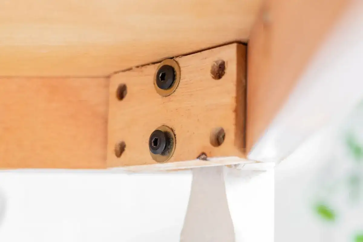 Close-up of wooden table joint with screws showing signs of loosened and weakened structural connection