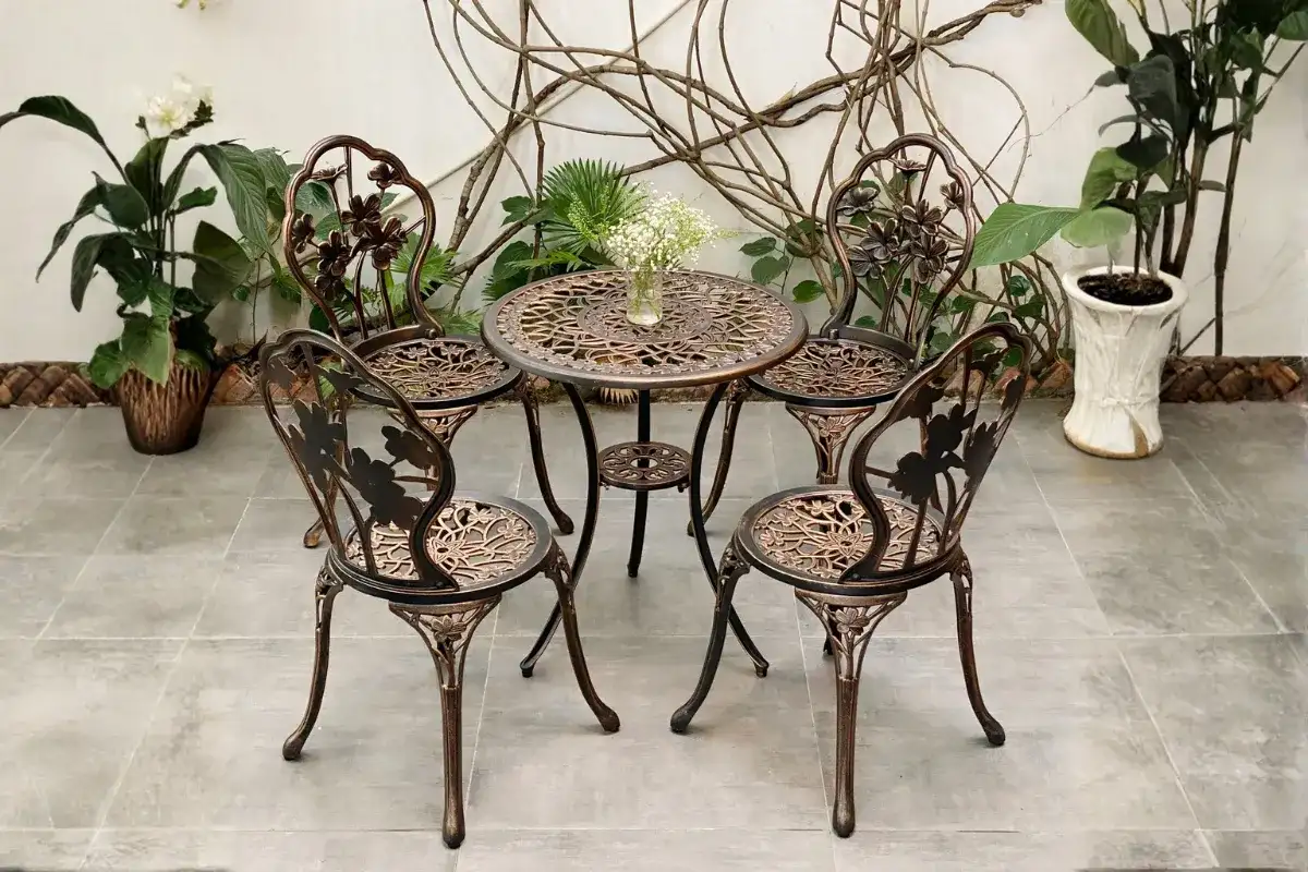 Bộ bàn ghế sắt nghệ thuật ngoài trời với hoa văn trang trí và bàn tròn đặt tại góc sân vườn