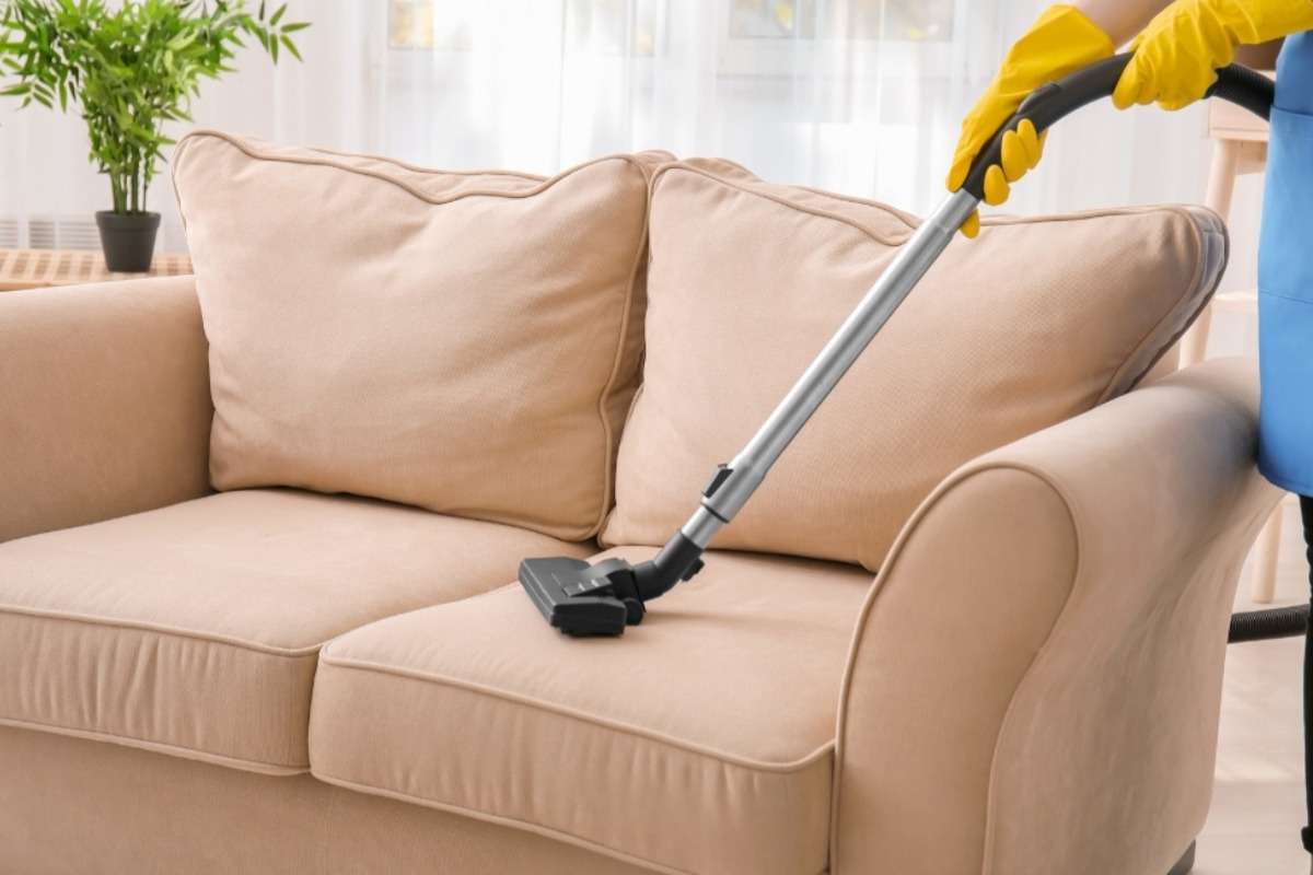 Person vacuuming a fabric 4-seater sofa as part of regular cleaning and upkeep.