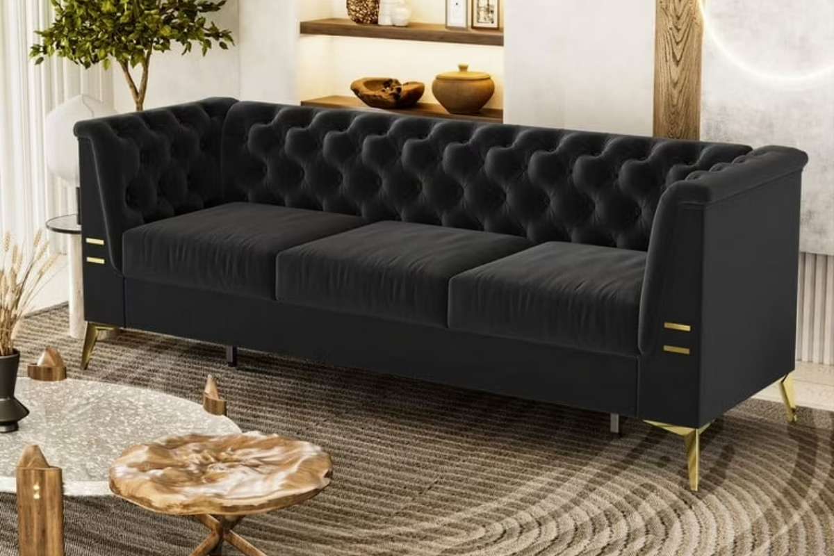  A black 3-seater sofa with tufted upholstery and gold accents placed in a modern living room.