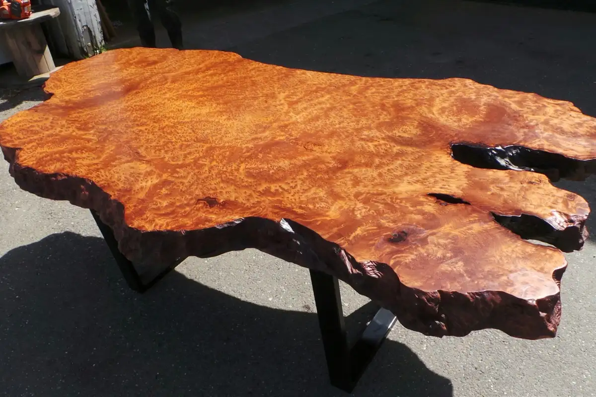Bàn nguyên tấm làm từ gỗ redwood tự nhiên, cạnh giữ nguyên dáng thô, vân gỗ nổi bật, được đặt ngoài trời dưới ánh nắng trực tiếp.