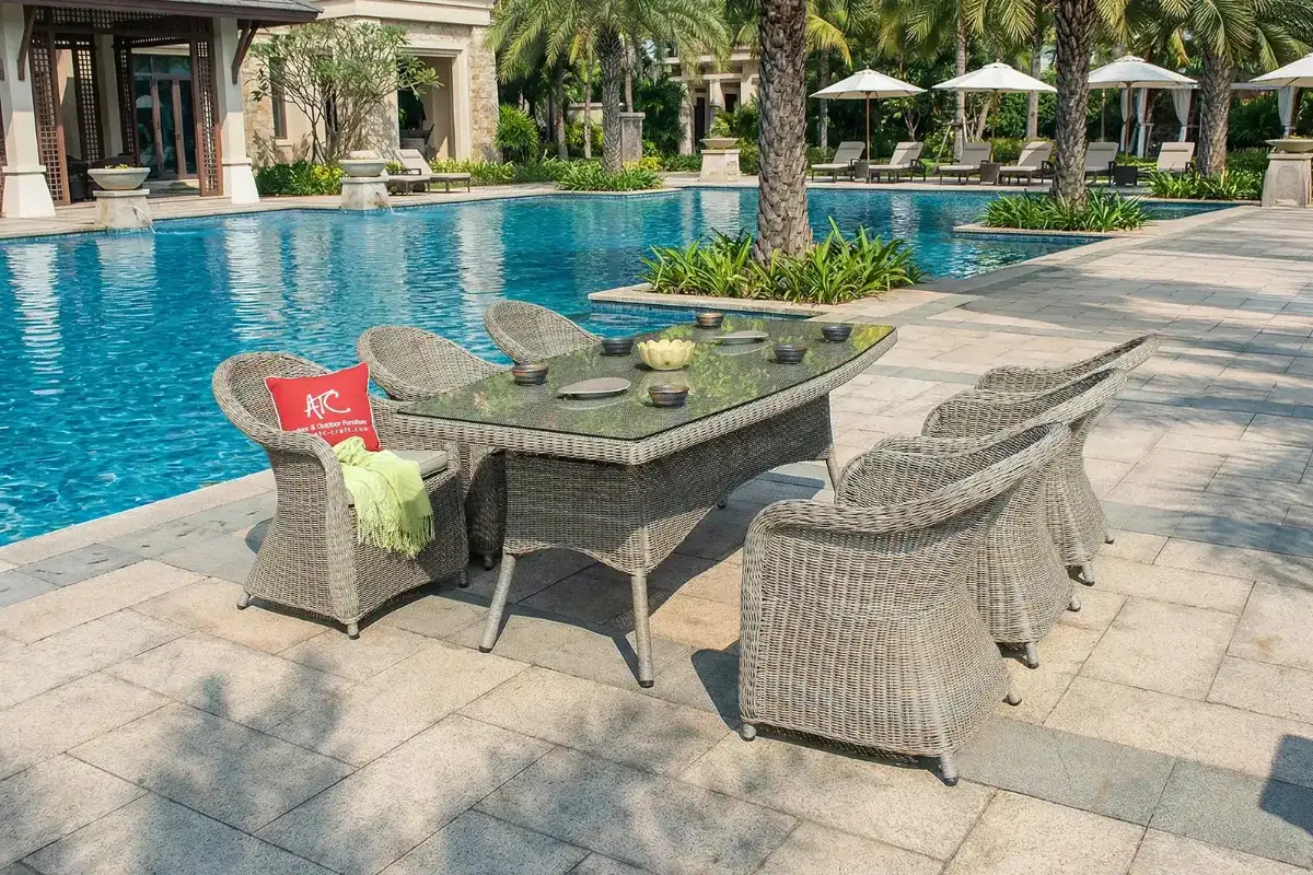 HARA 7-piece outdoor wicker dining set with a glass-top table and six chairs placed beside a resort-style swimming pool