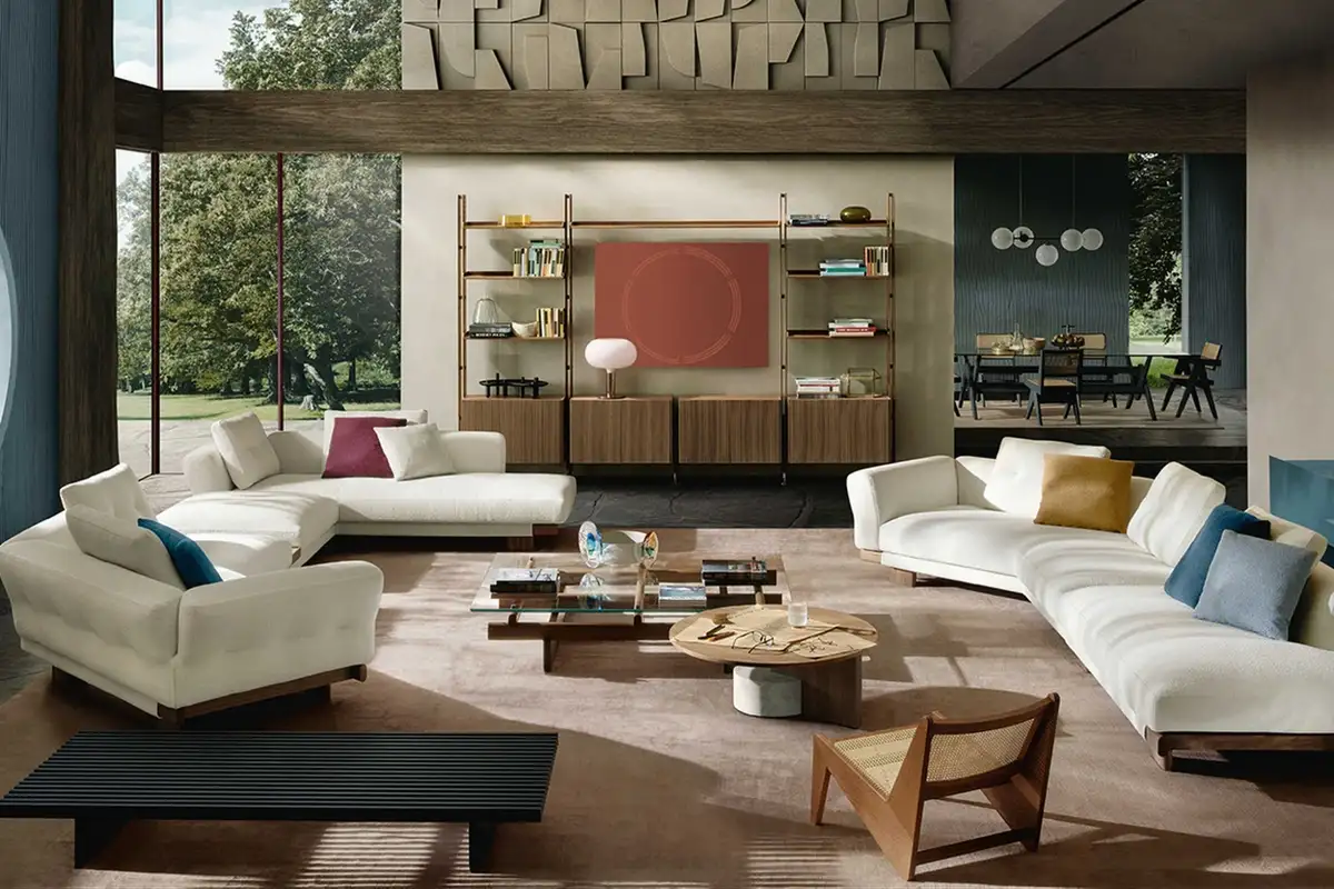 A spacious living room with white sofas, colorful cushions, wood accents, and large windows overlooking greenery, designed in a warm, modern style.
