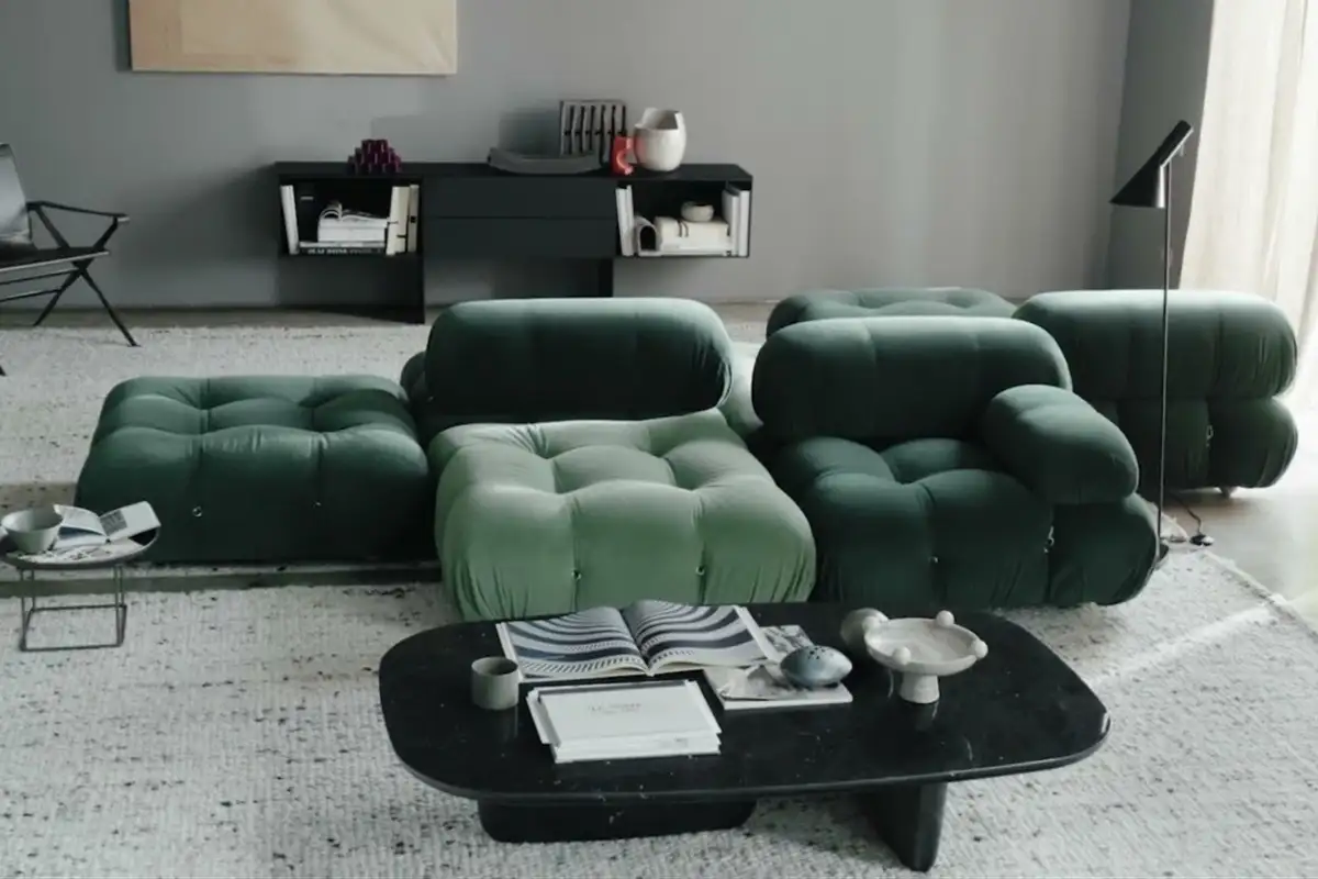 A chic living room with deep green modular sofas, a black coffee table, soft grey walls, and a cozy, minimalist vibe.