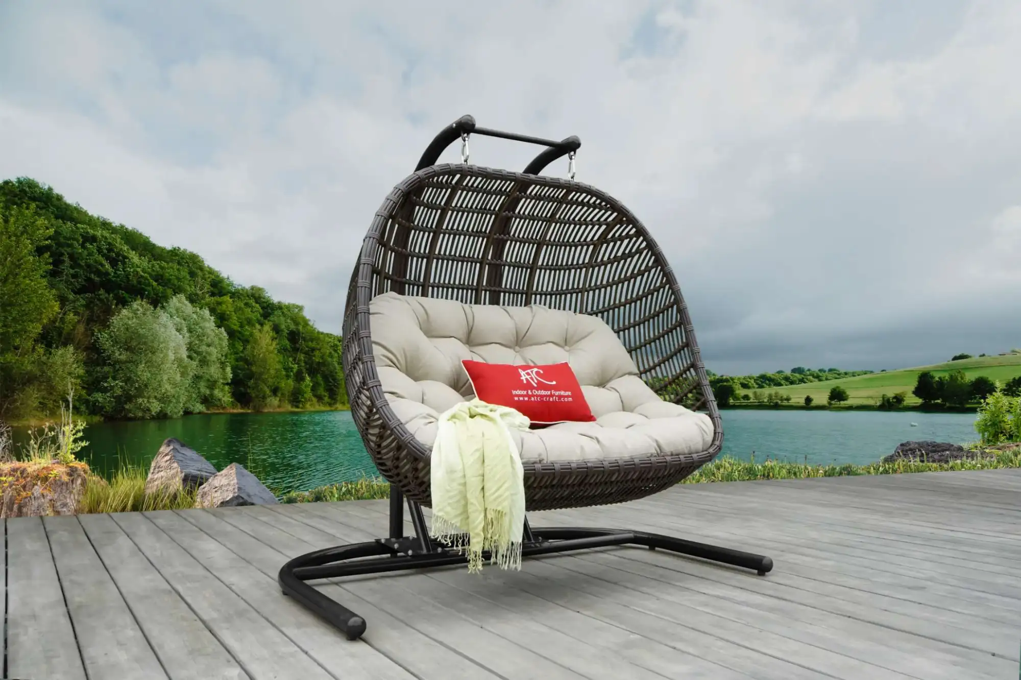 Outdoor synthetic rattan double egg chair on a wooden deck with natural landscape