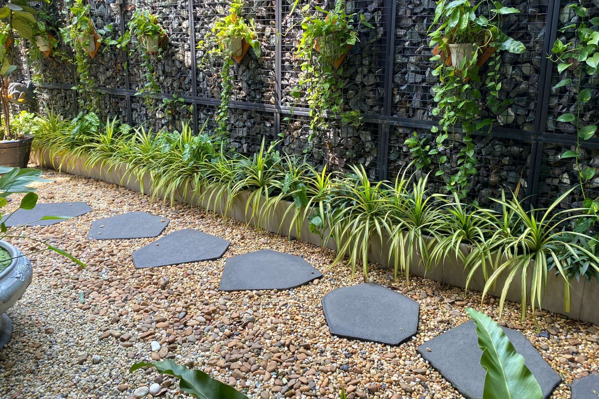 Gravel garden pathway with dark stepping stones, green border plants, and a decorative stone wall.