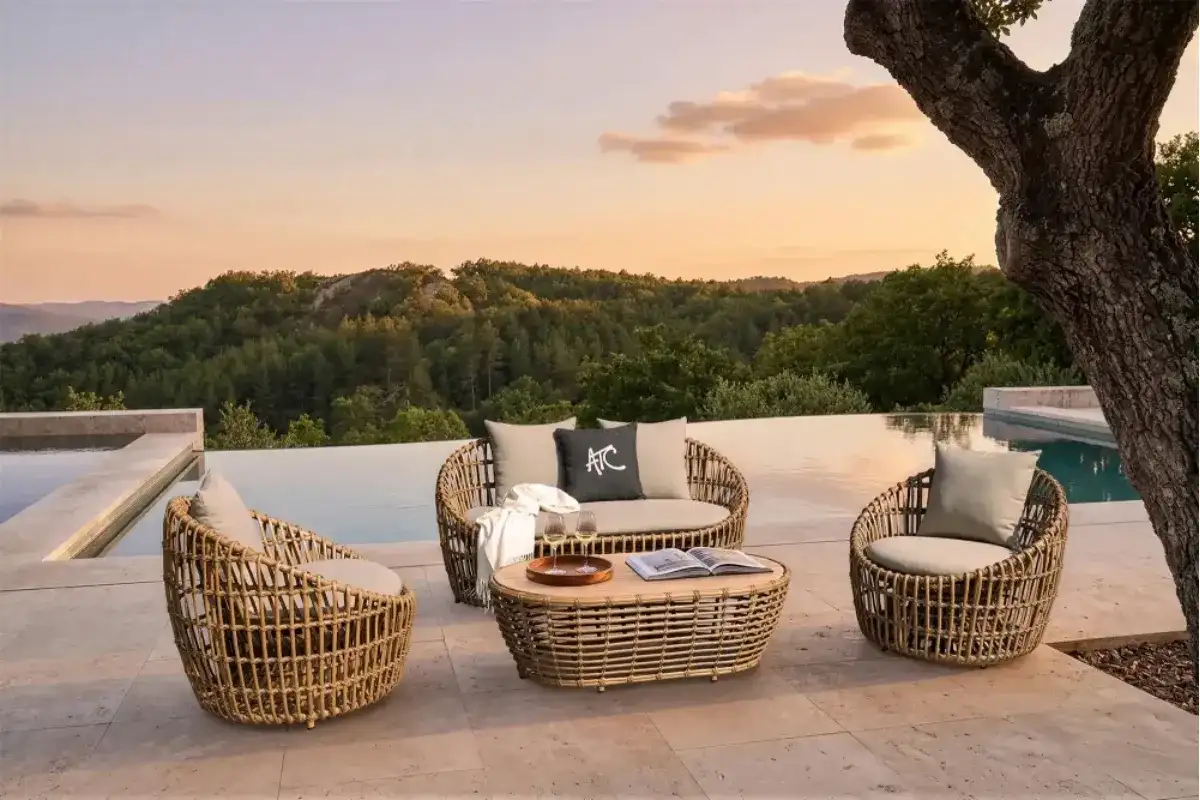 Bộ sofa ngoài trời mây nhựa với ghế tròn, bàn trà, đệm beige và khung cảnh hồ bơi nhìn ra núi lúc hoàng hôn