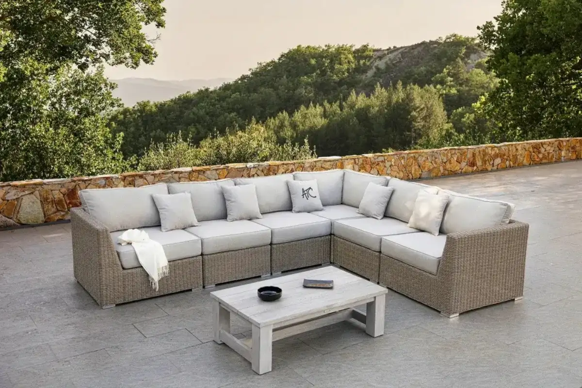 Bộ sofa góc mây nhựa chữ L PRESLEY-H với đệm beige và bàn trà đặt trên sân hiên rộng nhìn ra núi