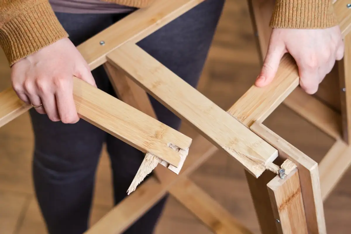 A person holding a broken wooden part of a furniture piece