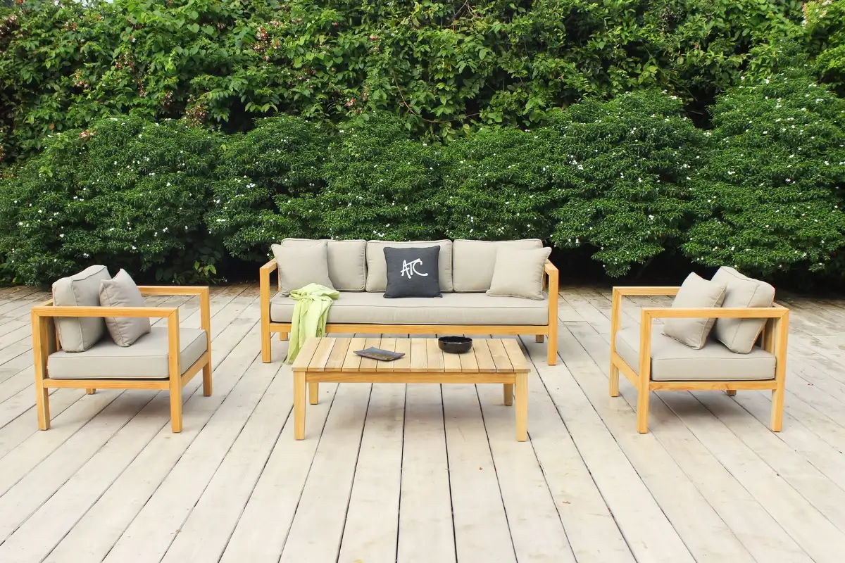 Outdoor teak wood sofa set including a coffee table, bench, and two single chairs placed on a wooden floor