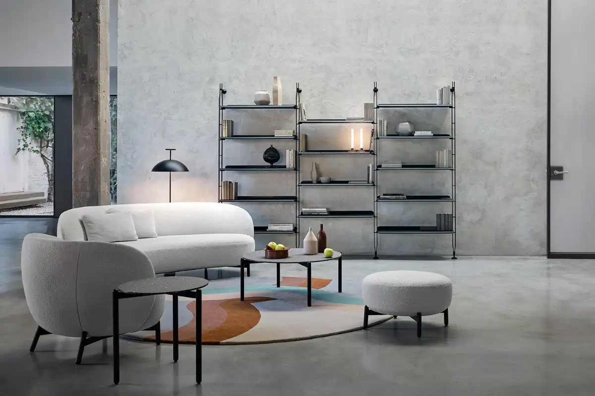 Phòng khách tối giản của Kartell với sofa trắng cong, thảm màu sắc tươi sáng, bàn tròn và kệ sách đen bóng