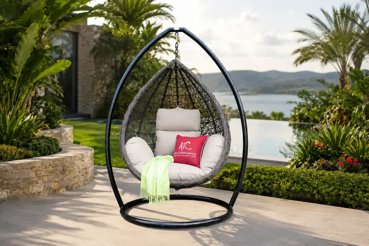 TROY teardrop outdoor swing chair with woven HDPE rattan frame and beige cushions in a luxury garden by the pool