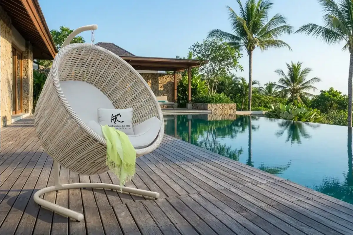 White outdoor hanging egg chair beside a villa pool with tropical palm trees
