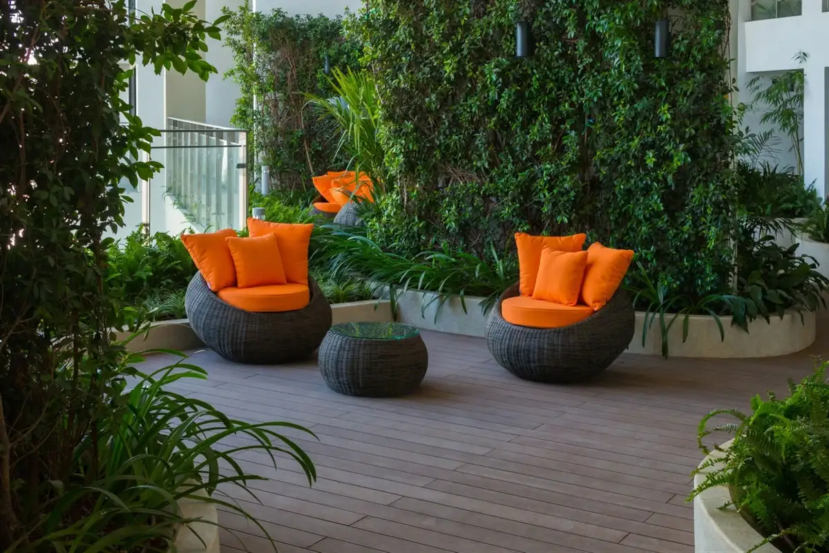 Bộ sofa ngoài trời dáng tròn với gối tựa cam nổi bật, đặt cạnh bức tường cây xanh, tạo không gian thư giãn hiện đại và sinh động.  