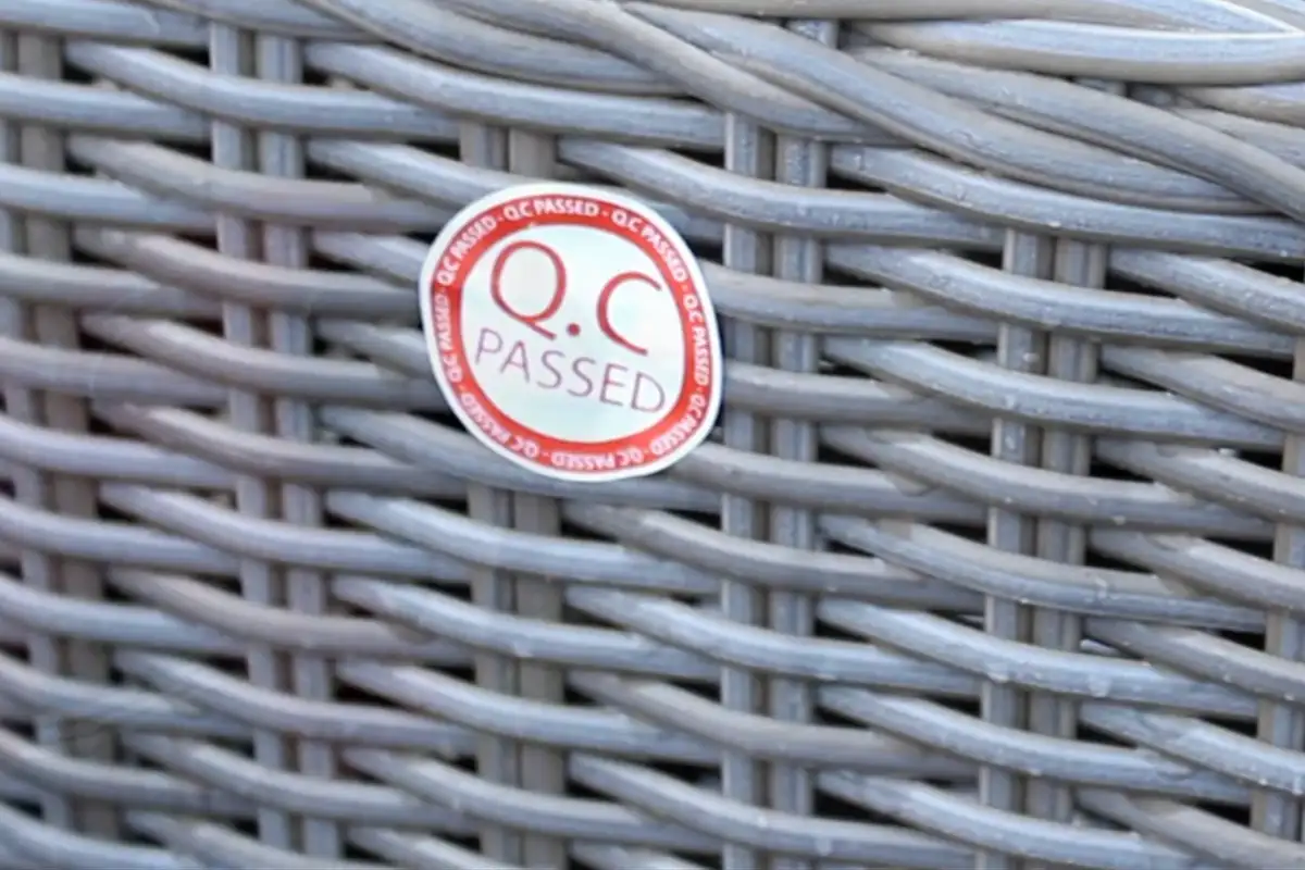 Tem kiểm định chất lượng "QC Passed" dán trên bề mặt mây nhựa đan ngoài trời, thể hiện quy trình kiểm soát chất lượng nghiêm ngặt.  