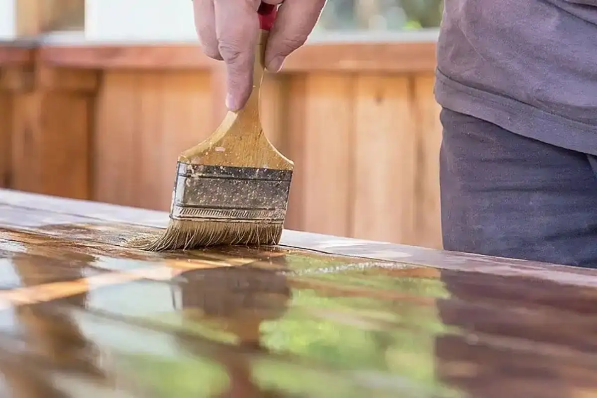 Applying protective oil to the surface of outdoor wooden furniture with a brush to enhance durability and protect against moisture.