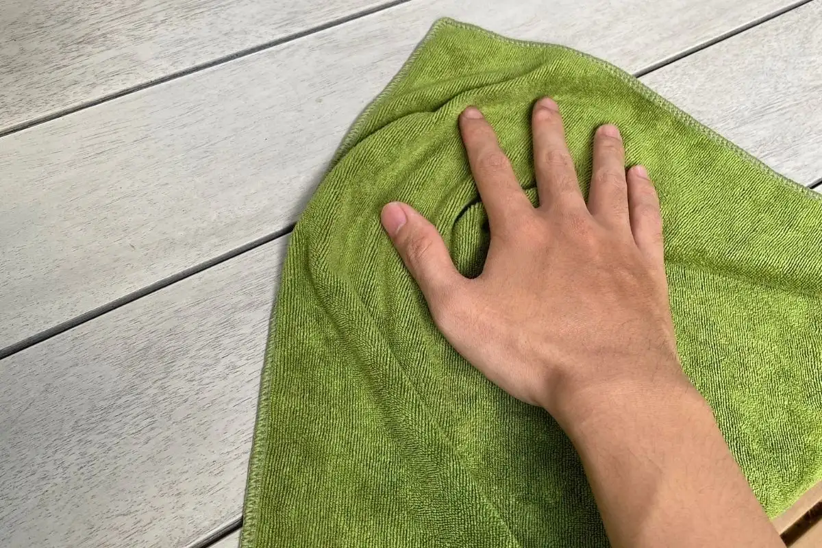 Hand cleaning the surface of a sustainable wood table with a green cloth, demonstrating proper cleaning methods for outdoor wooden furniture.