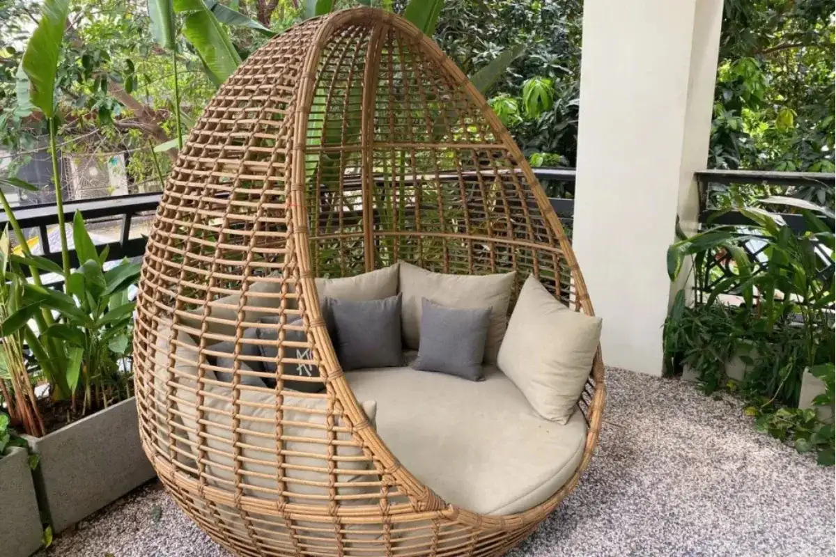 Outdoor wicker daybed placed in a mini garden corner with tropical plants and a relaxing natural setting