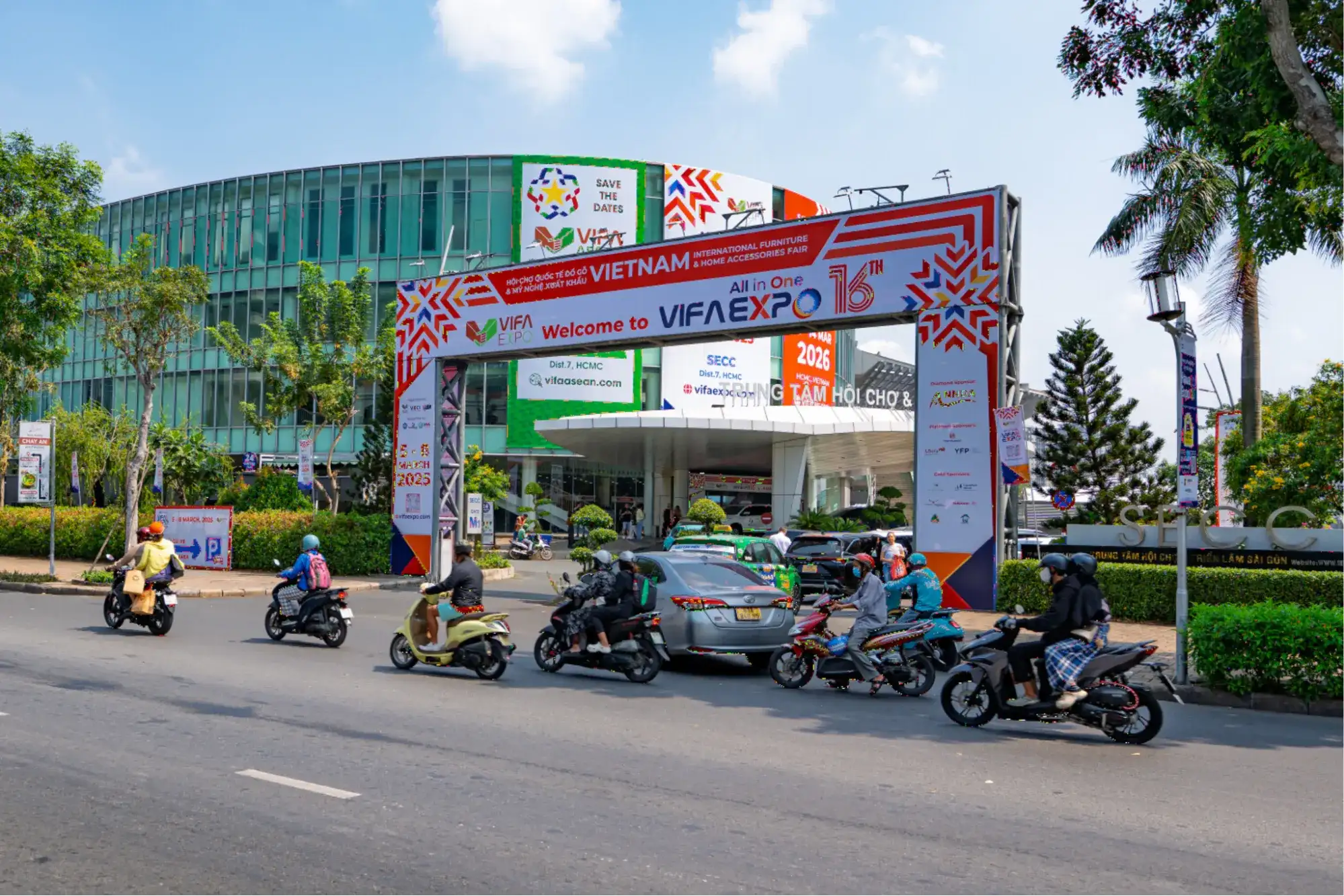 Main entrance of VIFA Expo in Ho Chi Minh City with large event signage, exhibition venue in the background, and busy street traffic in front.