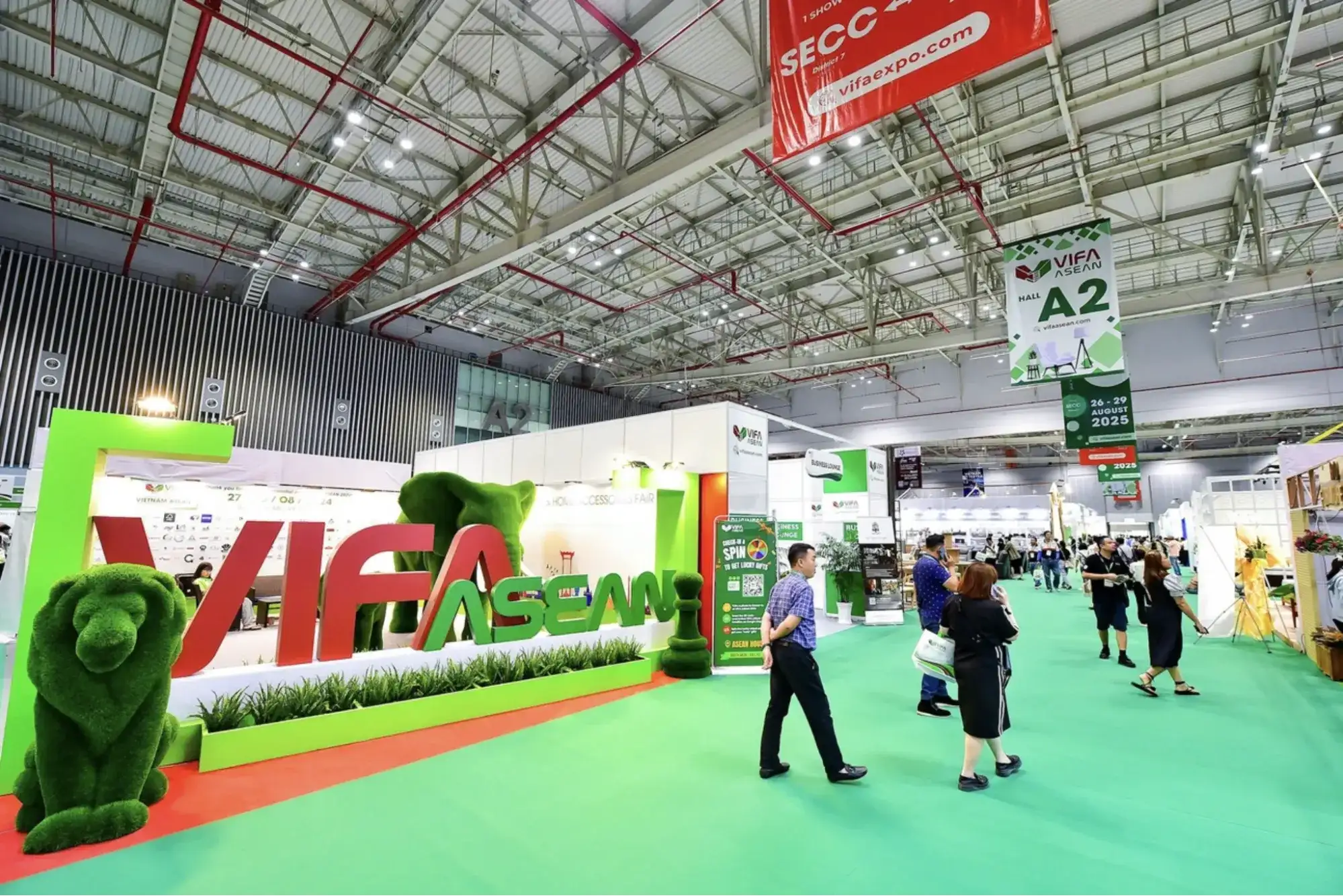 Entrance area of VIFA ASEAN exhibition at SECC with green carpeted aisles, branded signage, and buyers walking through furniture and home accessories booths.