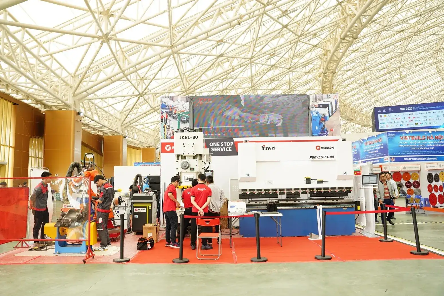 Crowded exhibition hall at Vietbuild Ho Chi Minh with construction material booths, interior products, and visitors walking through red-carpeted aisles.