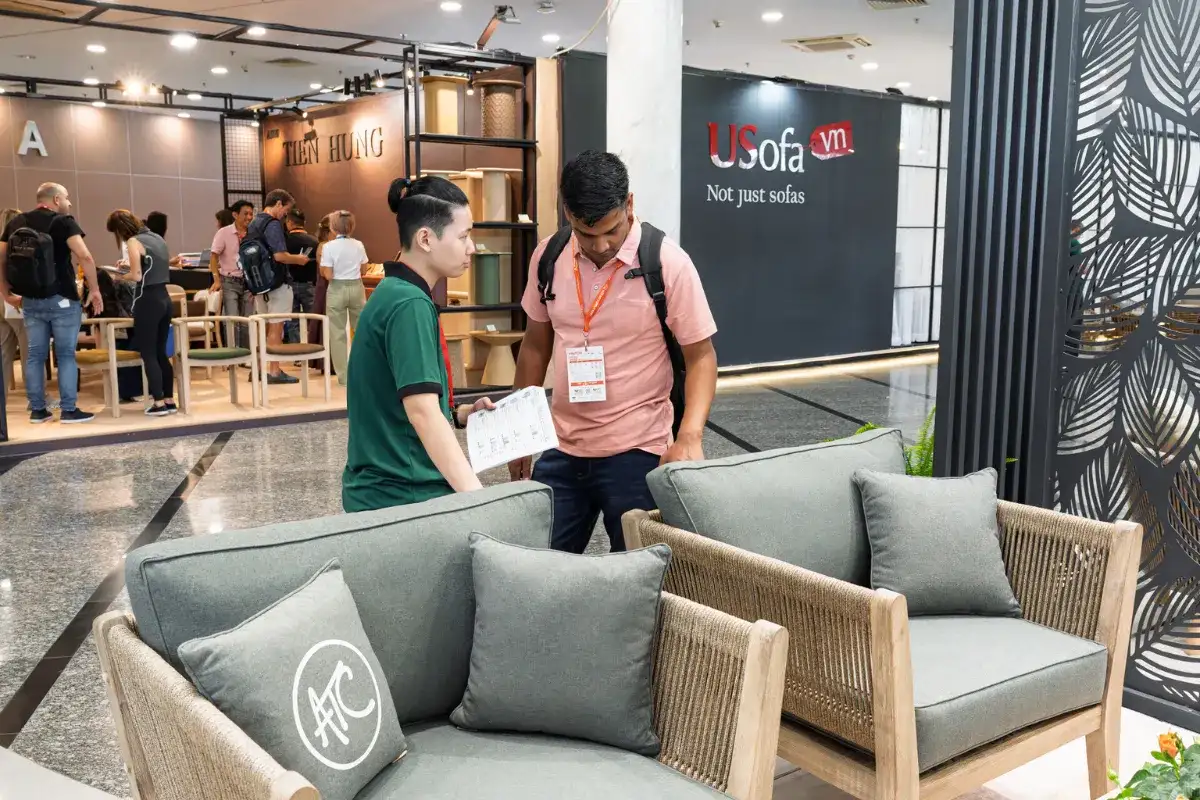 Buyer discussing product specifications with exhibitor at VIFA Expo while reviewing furniture display