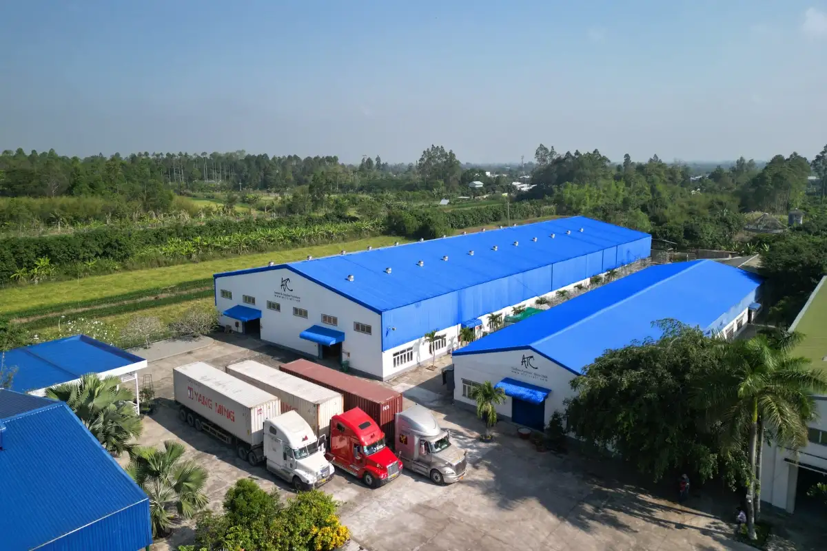 Overview of a large outdoor furniture factory with numerous container trucks and trucks parked in the loading area.