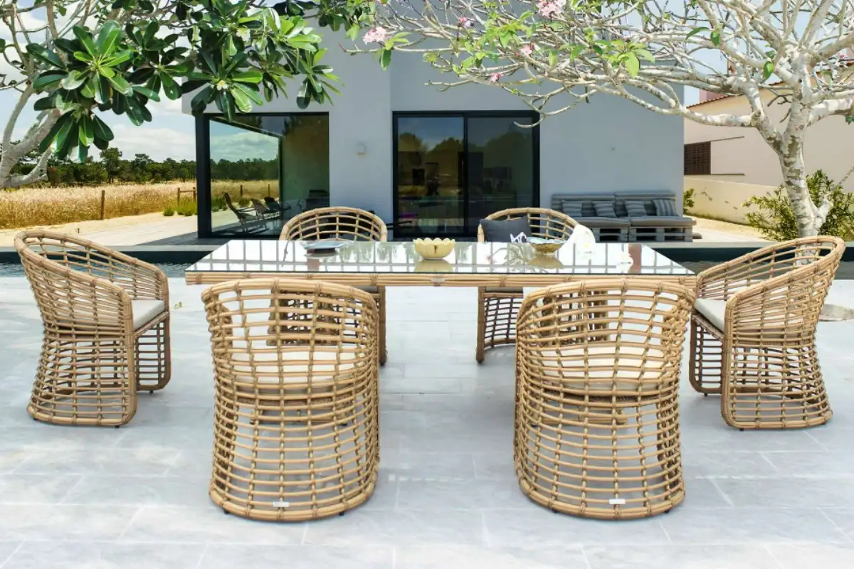 Outdoor dining set with light brown synthetic wicker frames and transparent glass tabletop on a spacious, airy terrace.