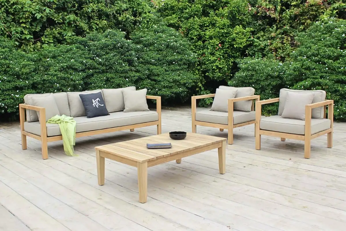 Bộ sofa ngoài trời bằng gỗ teak với đệm màu be, đặt trên sàn gỗ giữa không gian sân vườn