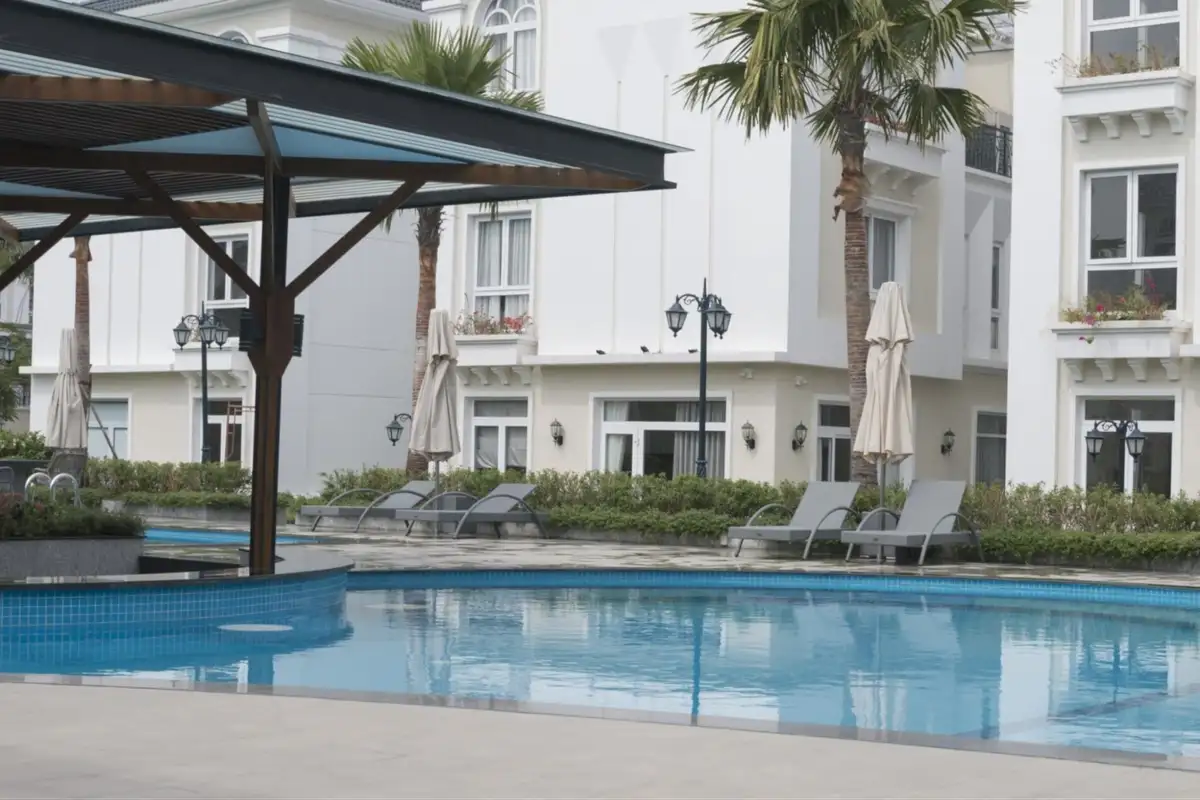 Poolside hotel area with outdoor rattan loungers and umbrellas, framed by palm trees and white modern buildings