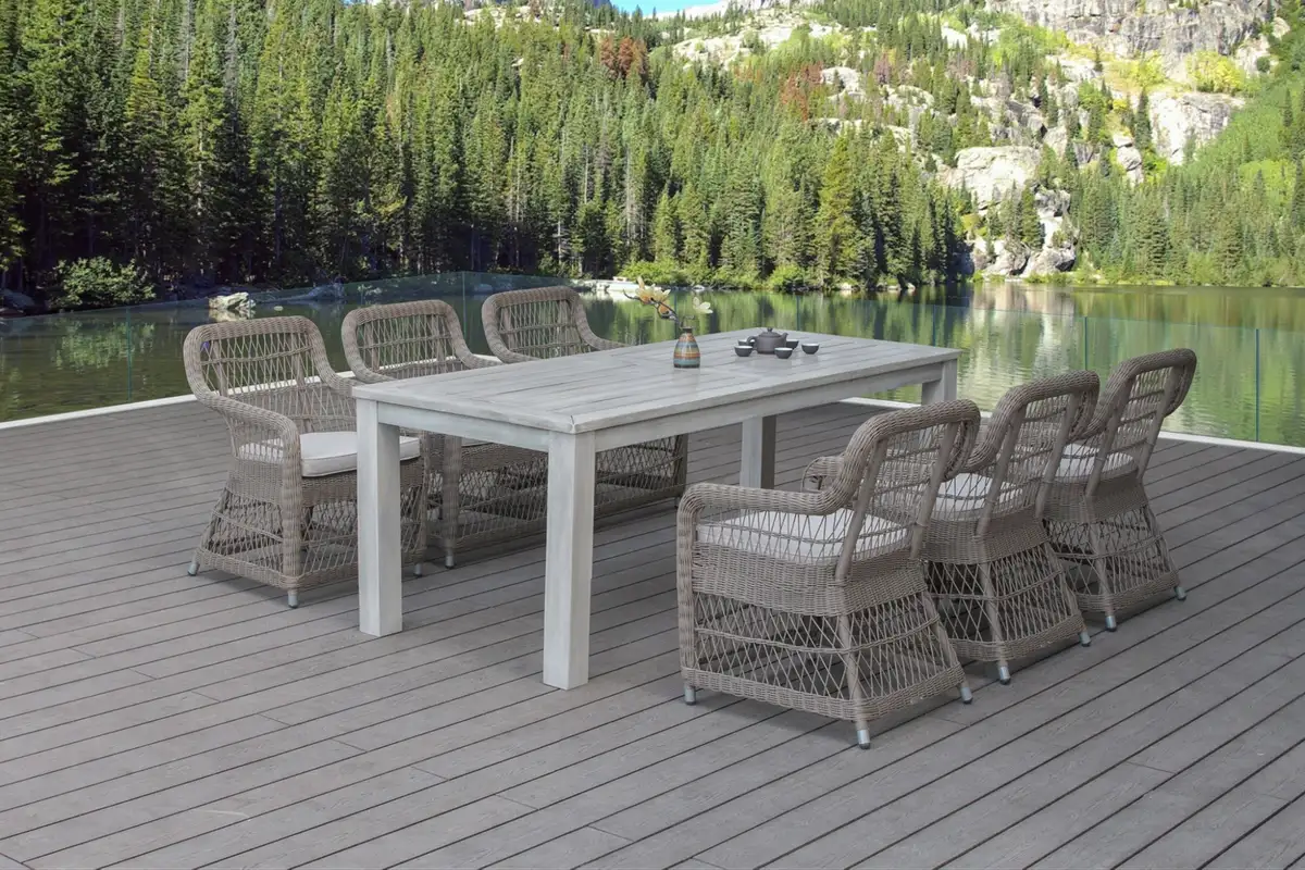 Outdoor dining set with woven HDPE rattan chairs and a teak-style table on a wooden deck by a scenic lake and pine forest