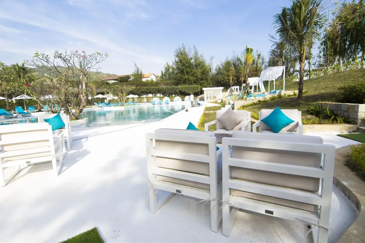 White outdoor lounge chairs with aqua cushions facing a poolside area in a resort surrounded by greenery