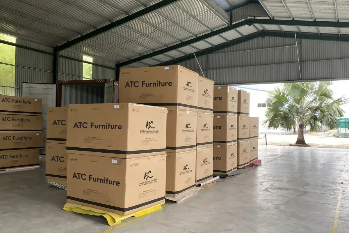 Stacks of packed ATC Furniture cartons ready for export in a covered warehouse area, positioned near a loading container