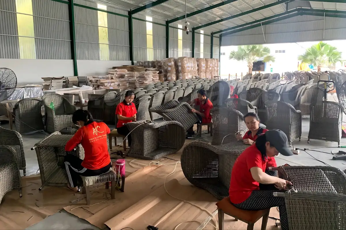 ATC Furniture’s skilled artisans hand-weaving rattan chairs inside the factory, surrounded by finished and semi-finished furniture pieces.