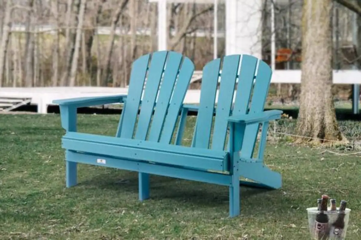 Blue double Adirondack chair with seating for two, placed outdoors on grass near trees.  