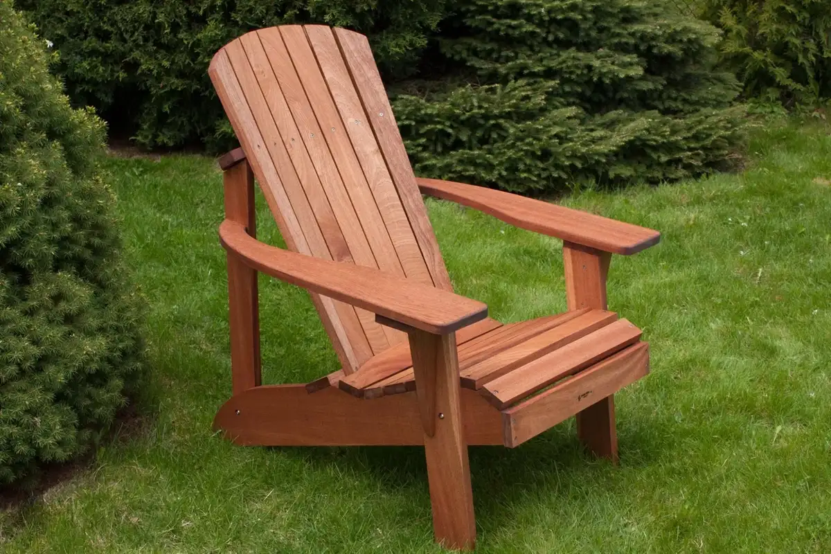 Wooden Adirondack chair placed on green grass with bushes in the background, highlighting its classic outdoor style.  