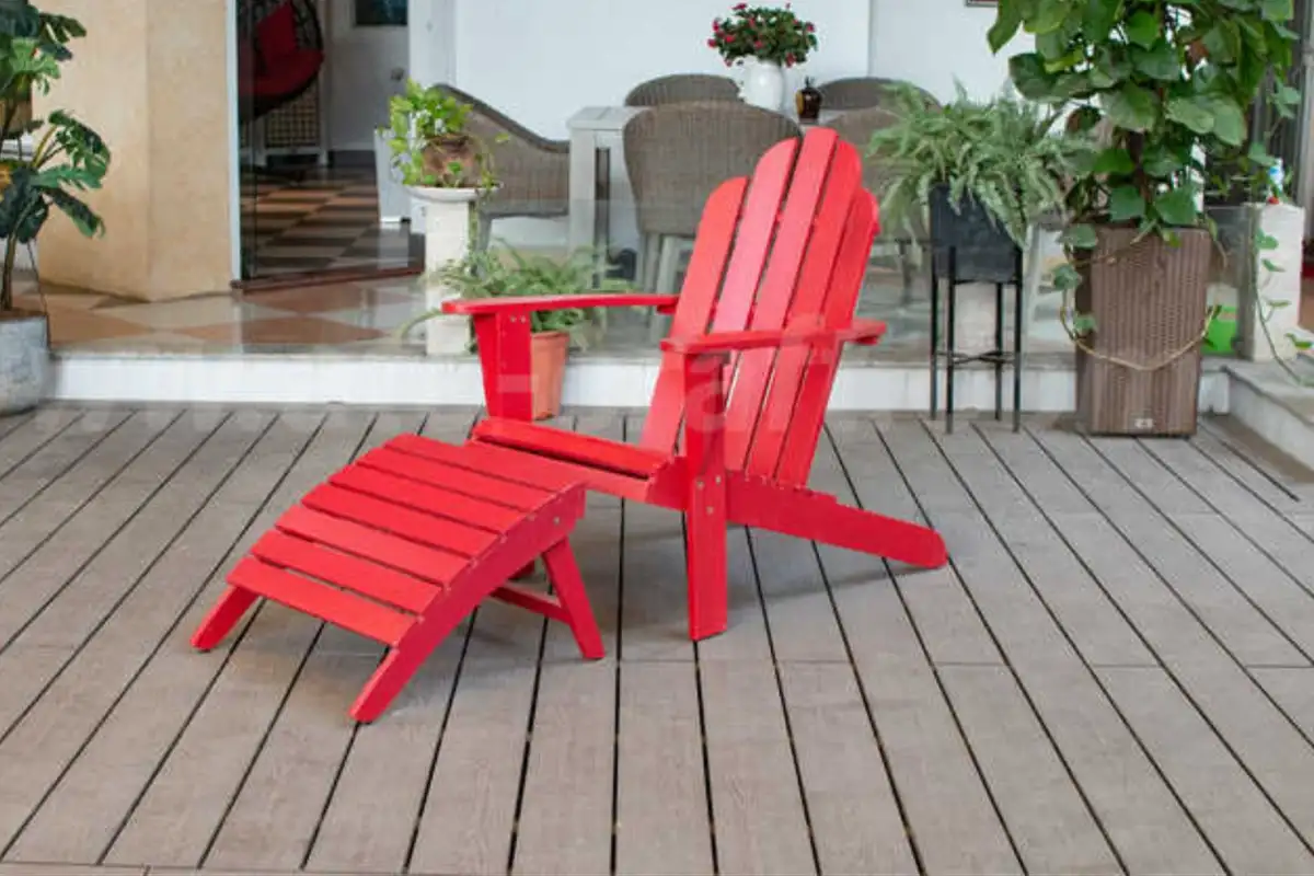 Red folding Adirondack chair with matching footrest on a wooden deck near potted plants and outdoor furniture.  