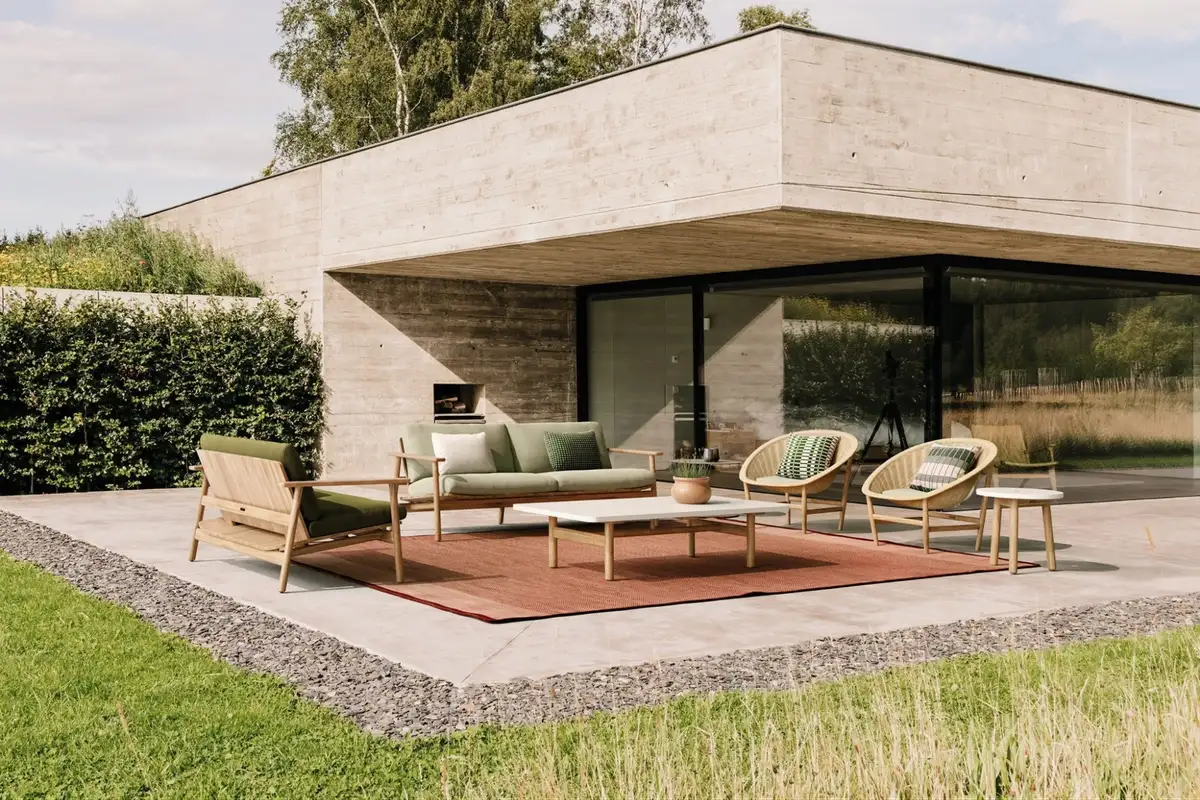 Minimalist outdoor sofa set with green cushions arranged on a patio outside a modern concrete house.  