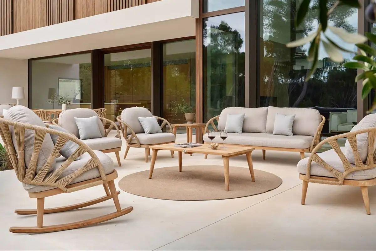 Modern patio seating arrangement with light gray cushions and natural wood frames in front of a villa.
