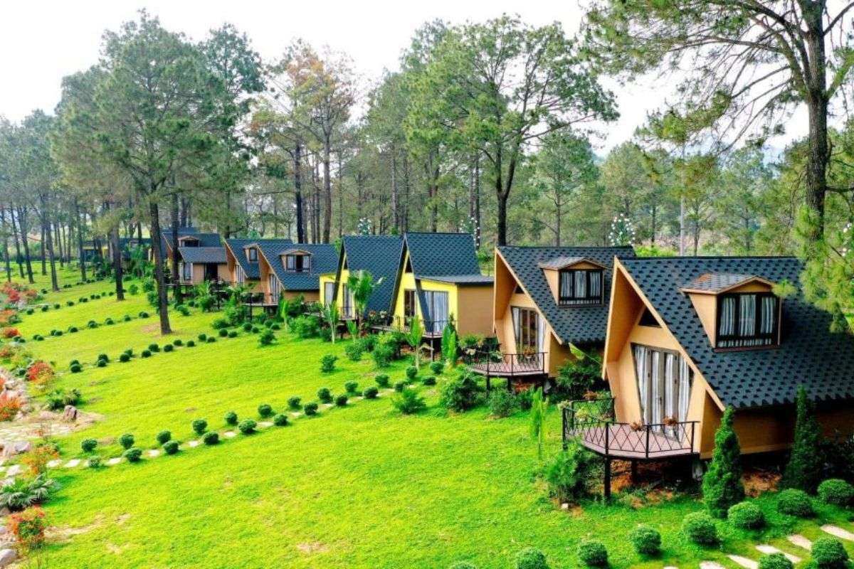 Resort garden with A-frame cabins, green sloped lawn, pine trees, trimmed shrubs, and private balconies