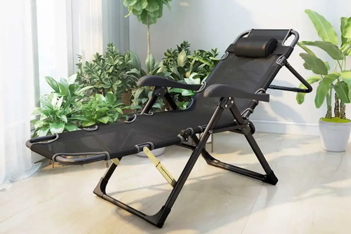 Ghế lười gấp gọn màu đen với khung ngả điều chỉnh đặt trong góc nhà sáng có cây xanh