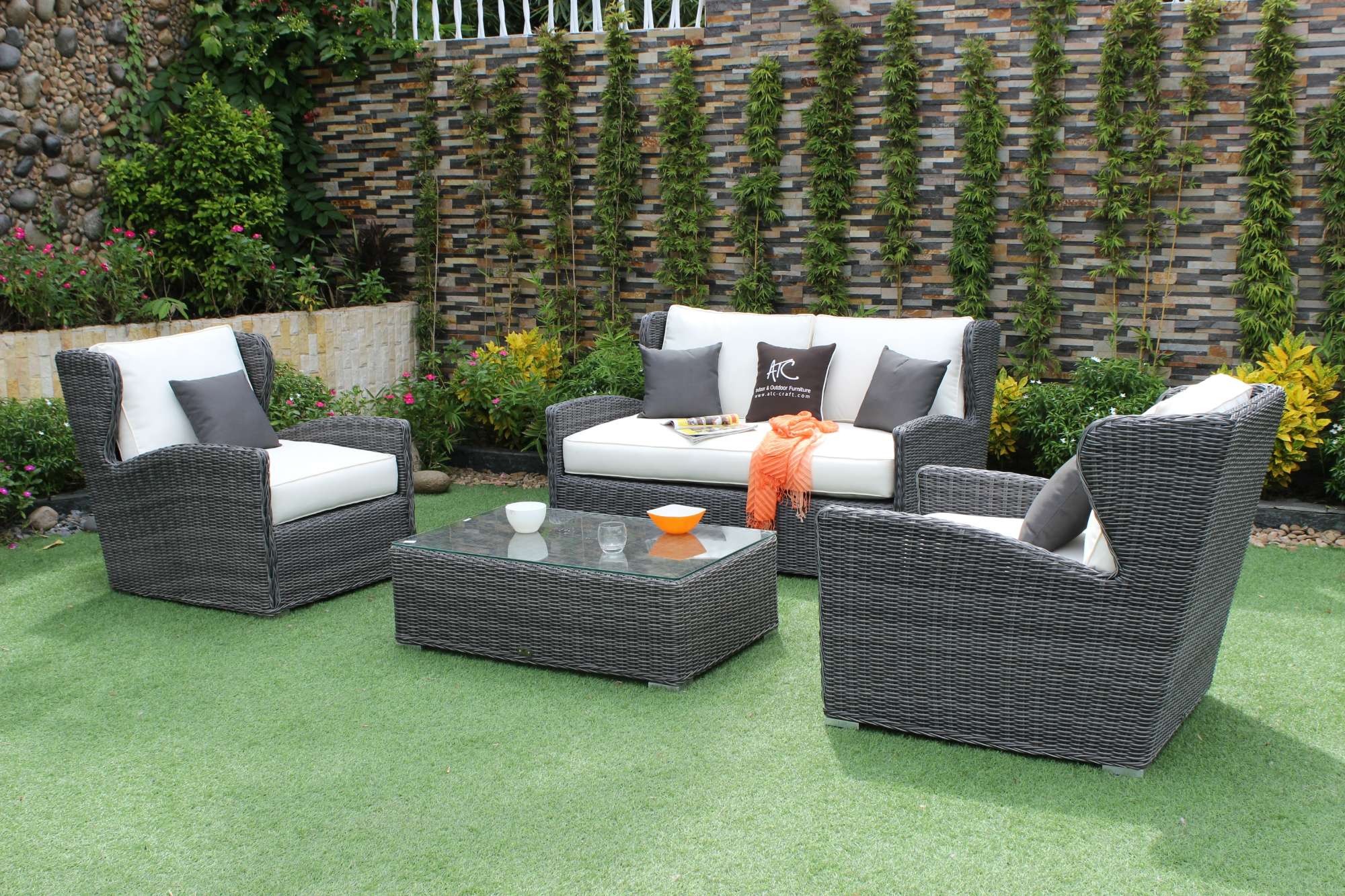 Black PE wicker sofa set with white cushions in a garden.