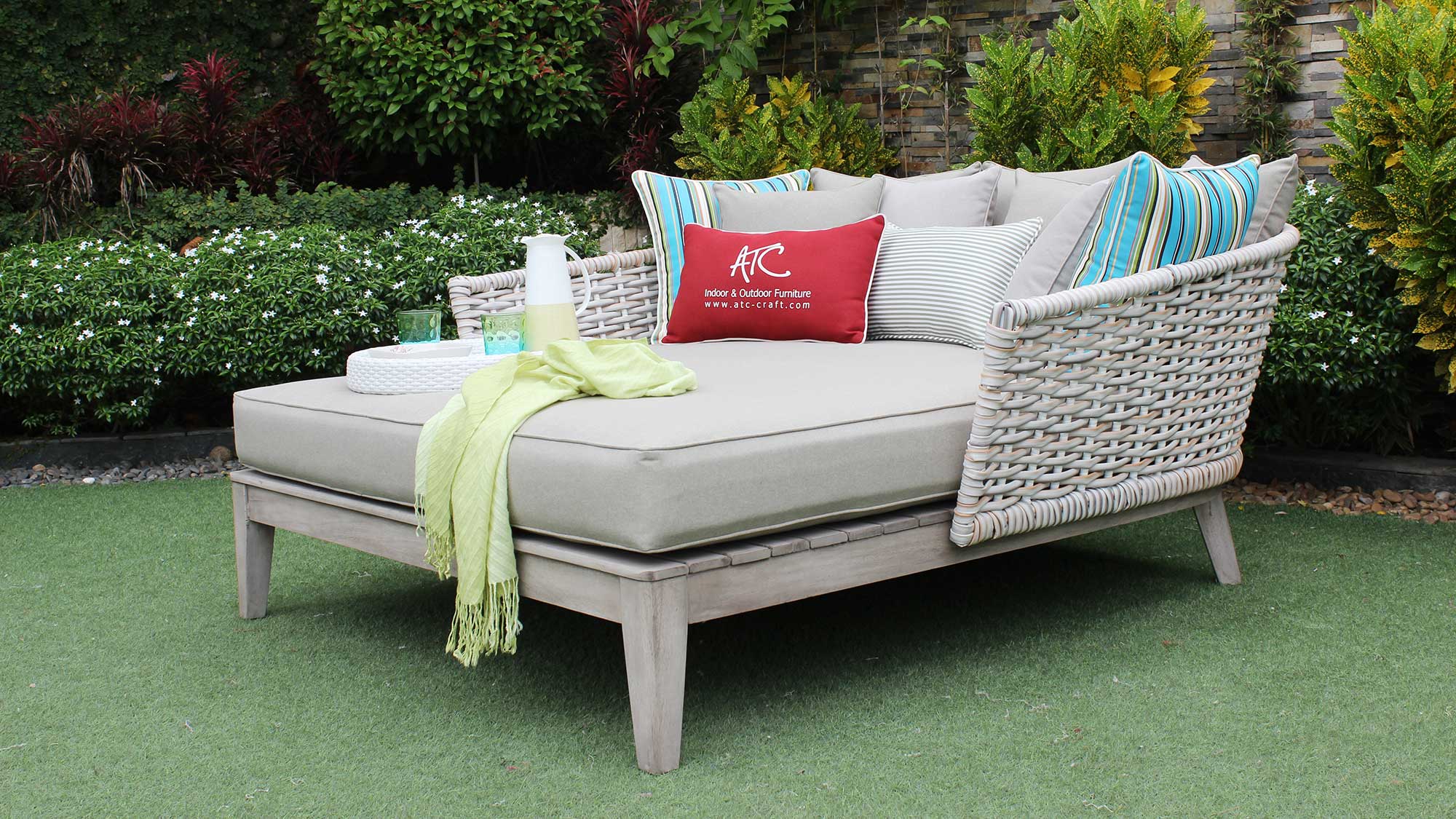 Neutral-tone PE wicker daybed in a lush garden setting.