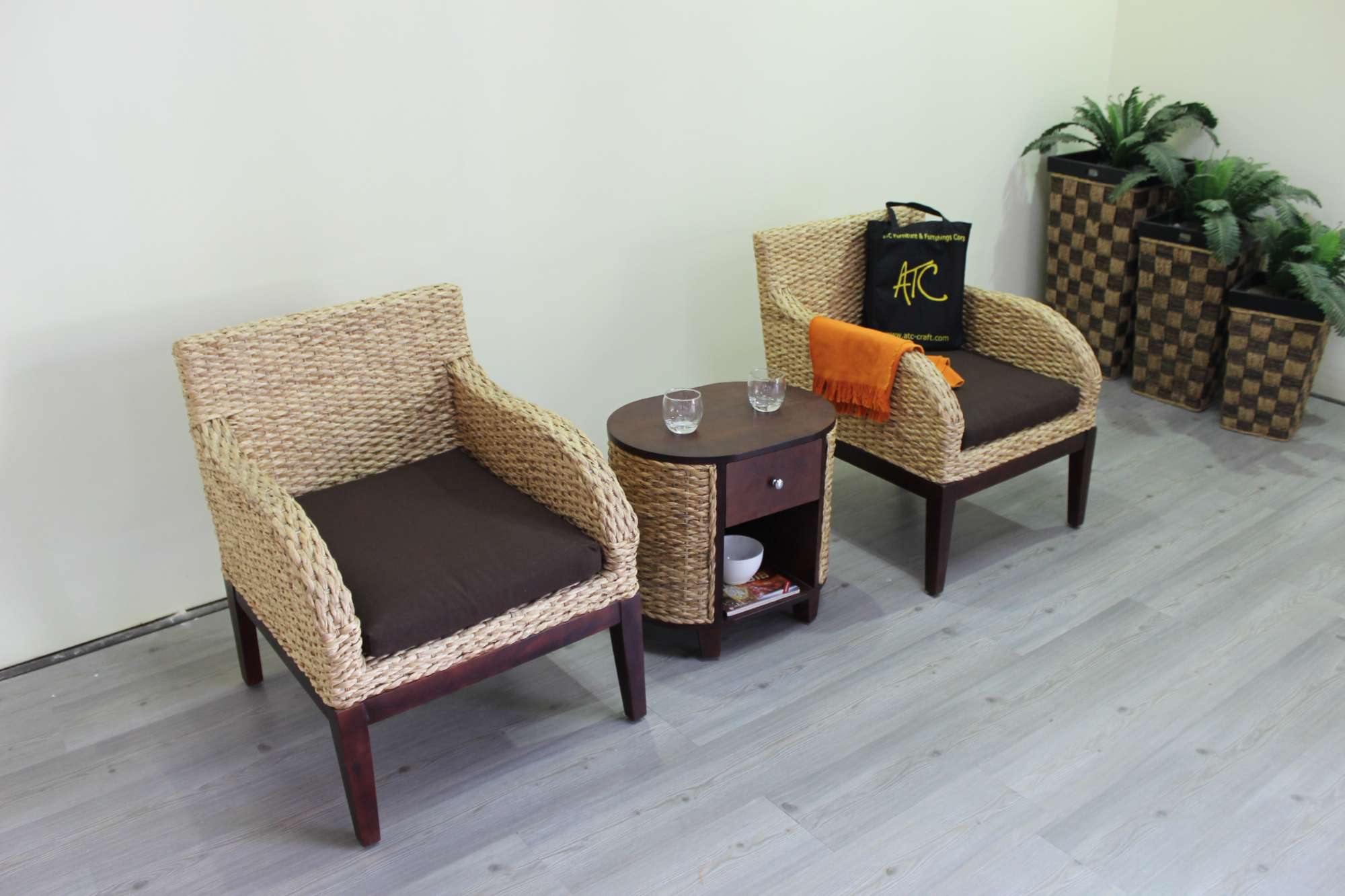 Natural rattan chairs with brown cushions and a small wooden table in a balcony corner.