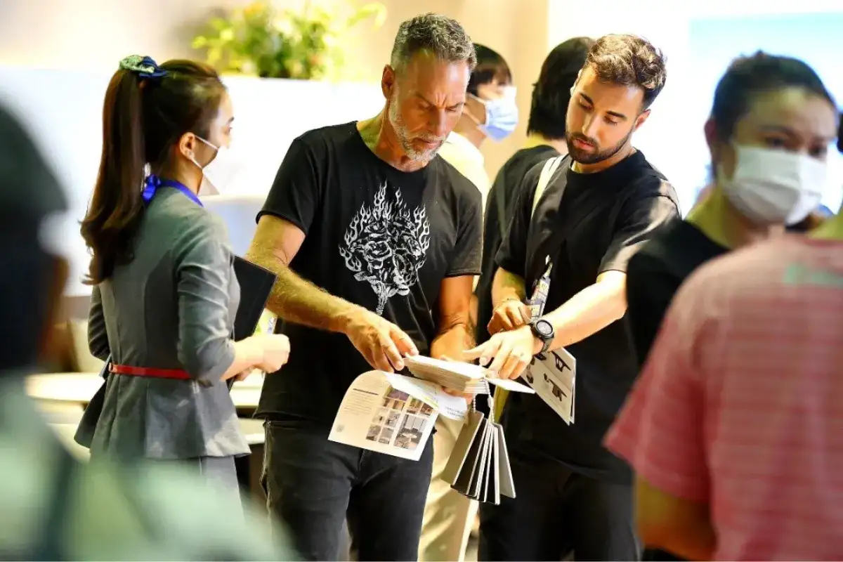 Foreign buyers and local representatives discussing furniture catalogs at a trade fair, highlighting how international importers connect with Quy Nhon furniture exporters.