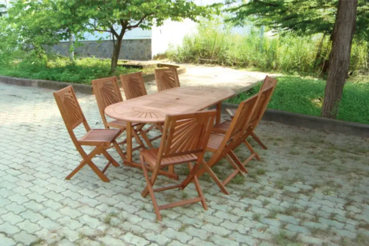 Wooden outdoor dining set with a large oval table and matching folding chairs, placed in a shaded garden area, representing Nghia Son’s durable and stylish furniture designs.