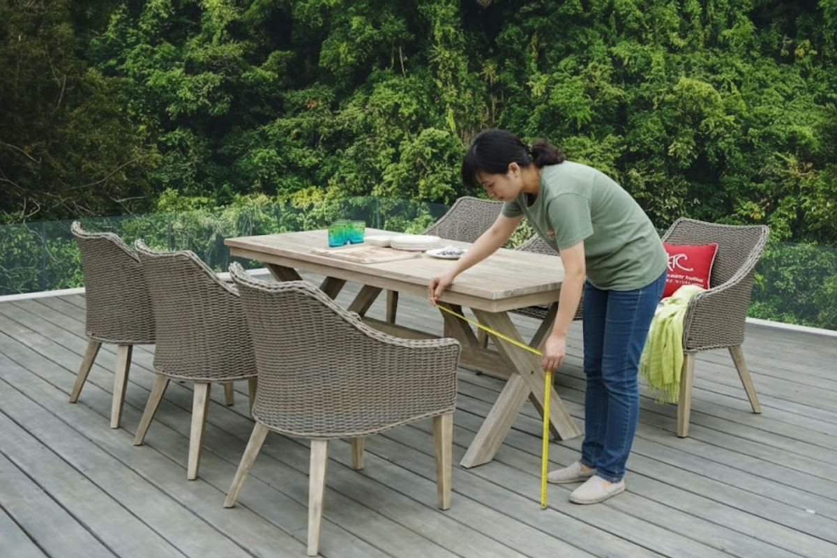 A woman measuring the space around a rattan dining table outdoors to ensure the right fit for the furniture.